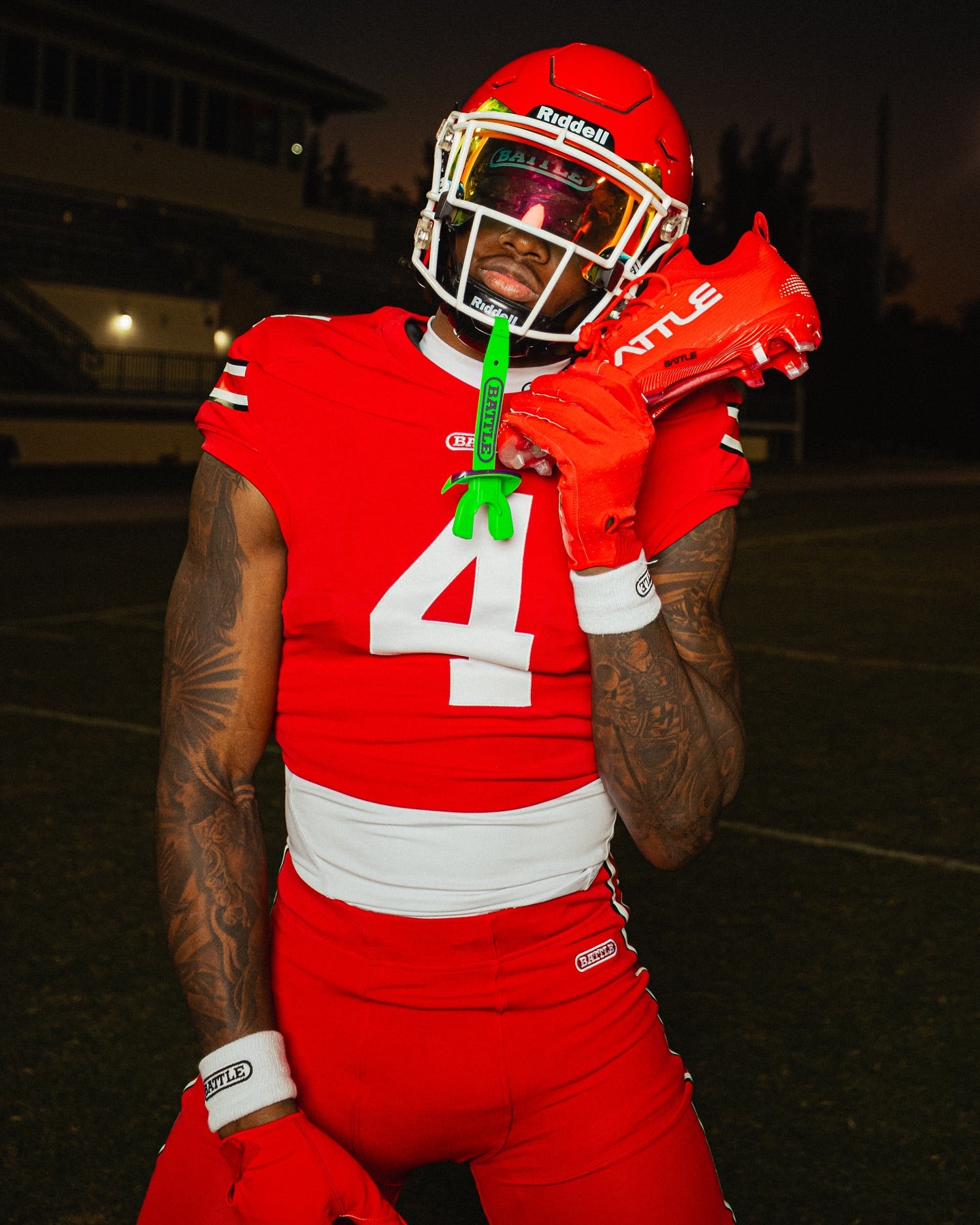 Person in red football uniform holding cleats on a dark field